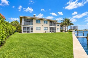 A two-story residential building with a well-maintained lawn and a dock extending into a body of water. - 2-bedroom 2- bath Waterfront Paradise With Intracoastal Views & Dock (West Palm Beach)