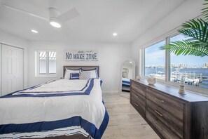 Een slaapkamer met een groot bed, een dressoir, een raam met uitzicht op het water en een bord aan de muur.