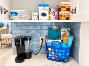 A kitchen counter with a coffee maker, a basket of colorful bath mats, and various kitchen supplies. - 2-bedroom 2- bath Waterfront Paradise With Intracoastal Views & Dock (West Palm Beach)