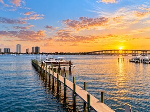 A waterfront scene with a wooden pier extending into calm waters, a bridge in the background, and high-rise buildings along the shore. - 2-bedroom 2- bath Waterfront Paradise With Intracoastal Views & Dock (West Palm Beach)
