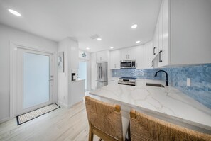 A modern kitchen with white cabinetry, stainless steel appliances, and a blue-tiled backsplash. - 2-bedroom 2- bath Waterfront Paradise With Intracoastal Views & Dock (West Palm Beach)