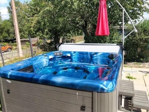 Ein Whirlpool mit blauer Außenhülle, einer Holzterrasse und einem roten Sonnenschirm.