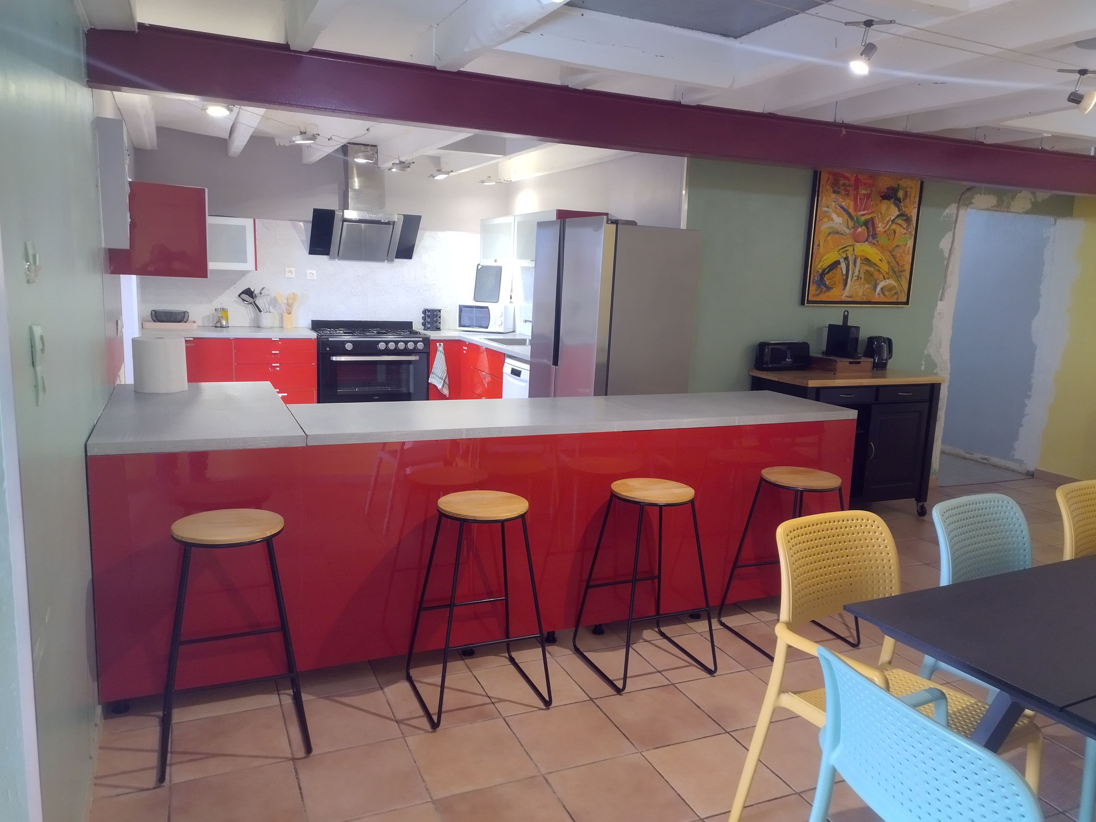 A kitchen with a red island, bar stools, and a dining area with chairs.