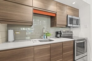 A modern kitchen with wooden cabinets, a stainless steel microwave, a coffee maker, and a built-in oven. - Remodeled 1BR · 5-Min Walk to Ski · Pool, Hot Tub, Sauna & Golf Views (Park City)