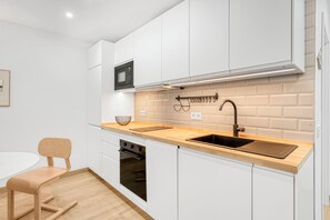 A modern kitchen with white cabinets, a wooden countertop, a black sink, and a microwave. - La Carihuela Seafront (Torremolinos)