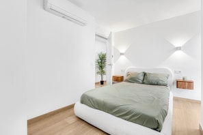 A modern bedroom with a bed, bedside tables, a wall-mounted light fixture, and a potted plant. - La Carihuela Seafront (Torremolinos)