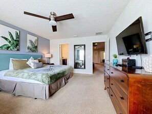Een slaapkamer met een bed, een dressoir, een televisie en een plafondventilator.