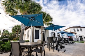 Outdoor seating with umbrellas, palm trees, and a building with a sign that reads 'The Cove Bar & Lounge'. - Disney 5BR Home, Private Pool, Water Slides (Kissimmee)
