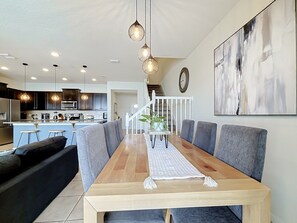 Een moderne eetruimte met een houten tafel, gestoffeerde grijze stoelen en hanglampen.