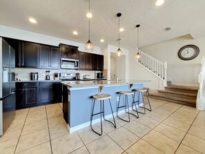 Une cuisine moderne avec des meubles de couleur sombre, un îlot central doté de tabourets et un escalier menant à un deuxième étage.
