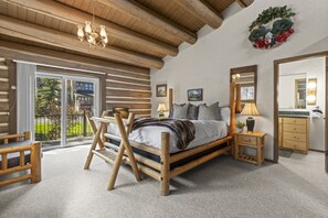 Un dormitorio de estilo cabaña de madera con cama, muebles de madera, un candelabro, un espejo y vistas al exterior.