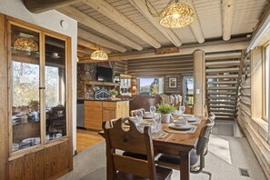 Uma área de refeições com mesa de madeira posta para seis pessoas, parede de pedra e televisão montada acima do balcão da cozinha.