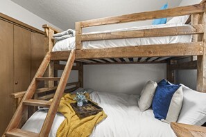 Una cama litera con escalera de madera, ropa de cama blanca y una manta amarilla.