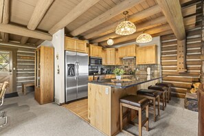 A log cabin-style kitchen with a stainless steel refrigerator, wooden cabinets, a central island with stools, and hanging pendant lights. - Private Hot Tub · Sleeps 10 · Under a 5-Minute Walk to Silver Star Lift (Park City)