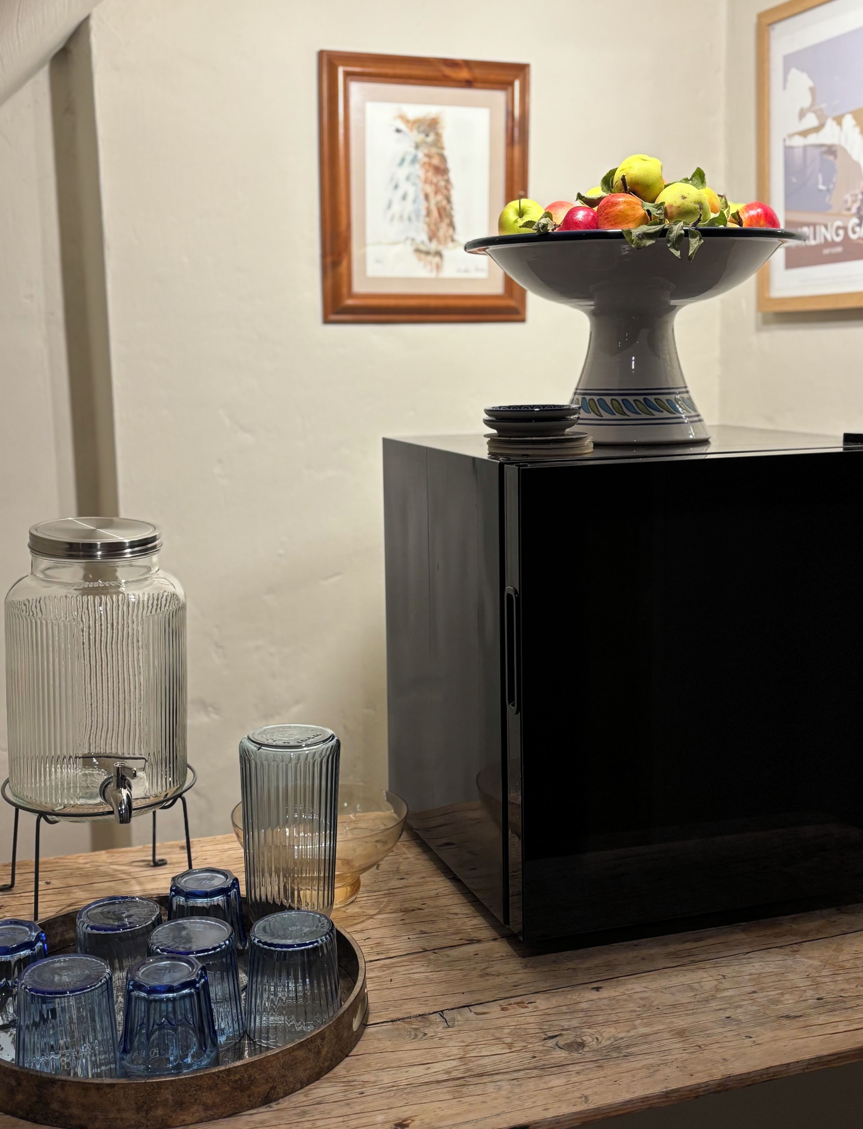 A kitchen counter with a fruit bowl, a glass jar, and a tray of blue glasses.