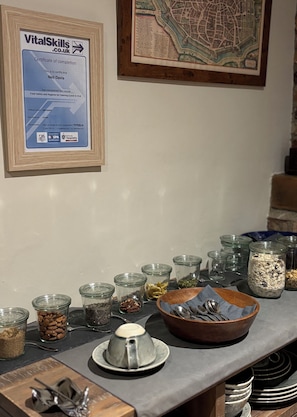 Una cuina amb un taulell ple d'aliments i utensilis, un certificat de finalització a la paret i un mapa emmarcat.