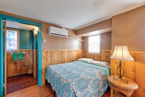 A bedroom with a bed, a bedside lamp, a window, an air conditioning unit, and a wooden door. - BC9--Studio Sleeps 2 Adults/2 Kids, Shared Pool/Hot Tub, Walk to Beach, Dogs OK! (Port Aransas)