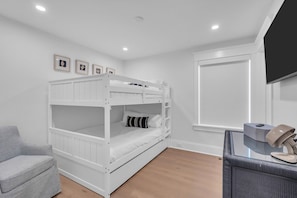 A bunk bed with white bedding, a grey armchair, a television, and a window with blinds. - Luxury 5BR | Sleeps 16 | 1 Block to Beach & Boardwalk (Ocean City)