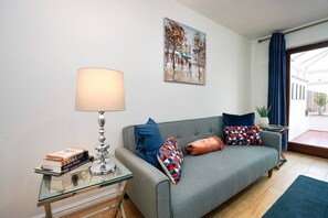 A living room with a grey sofa, a glass coffee table with books, a lamp, and a painting on the wall. - 2-bed Cambridge house with garden and parking for 2 cars (Fulbourn)