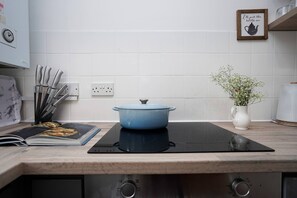 Cuina amb una olla blava sobre una fogairella d'inducció, un vas de flors blanc i un quadre penjat a la paret.