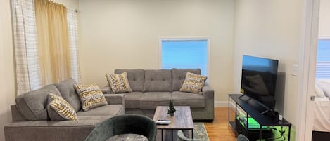 A living room with a sectional sofa, two armchairs, a coffee table, a TV, and a small table with a plant.