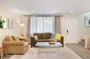 A living room with a sofa, a coffee table, and a lamp. There is a door and a staircase visible in the background. - Cozy 3-bedroom townhome with fireplace and AC in lovely Bellevue (Bellevue)