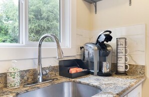Eine Küche mit Spüle aus Edelstahl, einer Kaffeemaschine, einem Toaster und einem Beistellregal für Tassen.