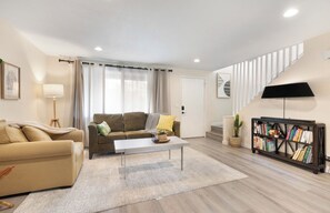 Ein Wohnzimmer mit Sofa, Couchtisch, Bücherregal und Treppe.