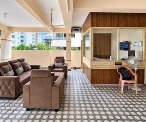 Eine Hotelhalle mit einer Rezeption, einer Sitzecke mit Sofas, einem gemusterten Boden und einem Deckenventilator.