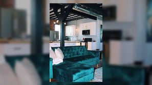 A room with a teal velvet sofa, a kitchen area with white cabinets, and a modern ceiling with exposed beams and ductwork. - Beautiful 4-Bed Loft in the heart of Festus Main St (Festus)