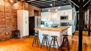 A kitchen with a central island, bar stools, and a brick wall. - Beautiful 4-Bed Loft in the heart of Festus Main St (Festus)