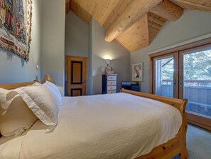 Un dormitorio con una cama de madera, una mesita de noche, un aparador y una ventana con vista a árboles.