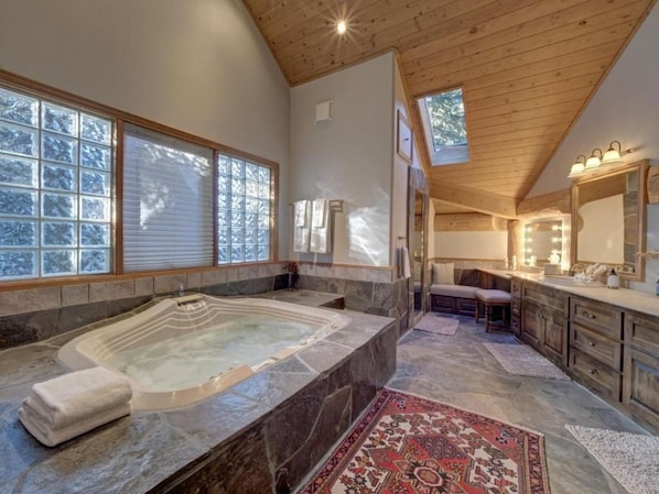 Un baño con una bañera grande, un tocador con espejo y una ventana con persianas.