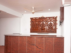 A reception area with a wooden decorative panel, a ceiling fan, and a tiled counter. - Classic Hotel Aiswariyam (Puducherry)