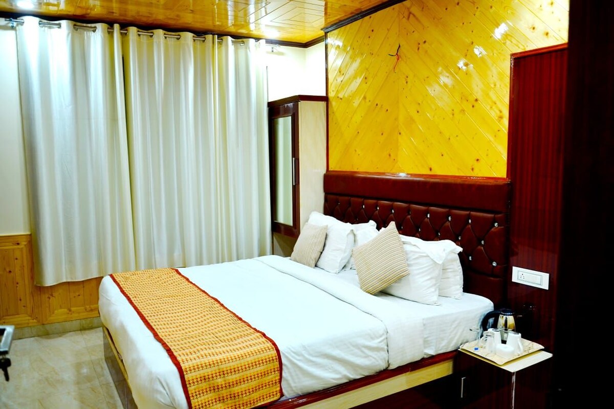 Ein Hotelzimmer mit einem großen Bett, einem Holzkopfstück, einem Nachttisch mit Lampe und einem Fenster mit Vorhängen.