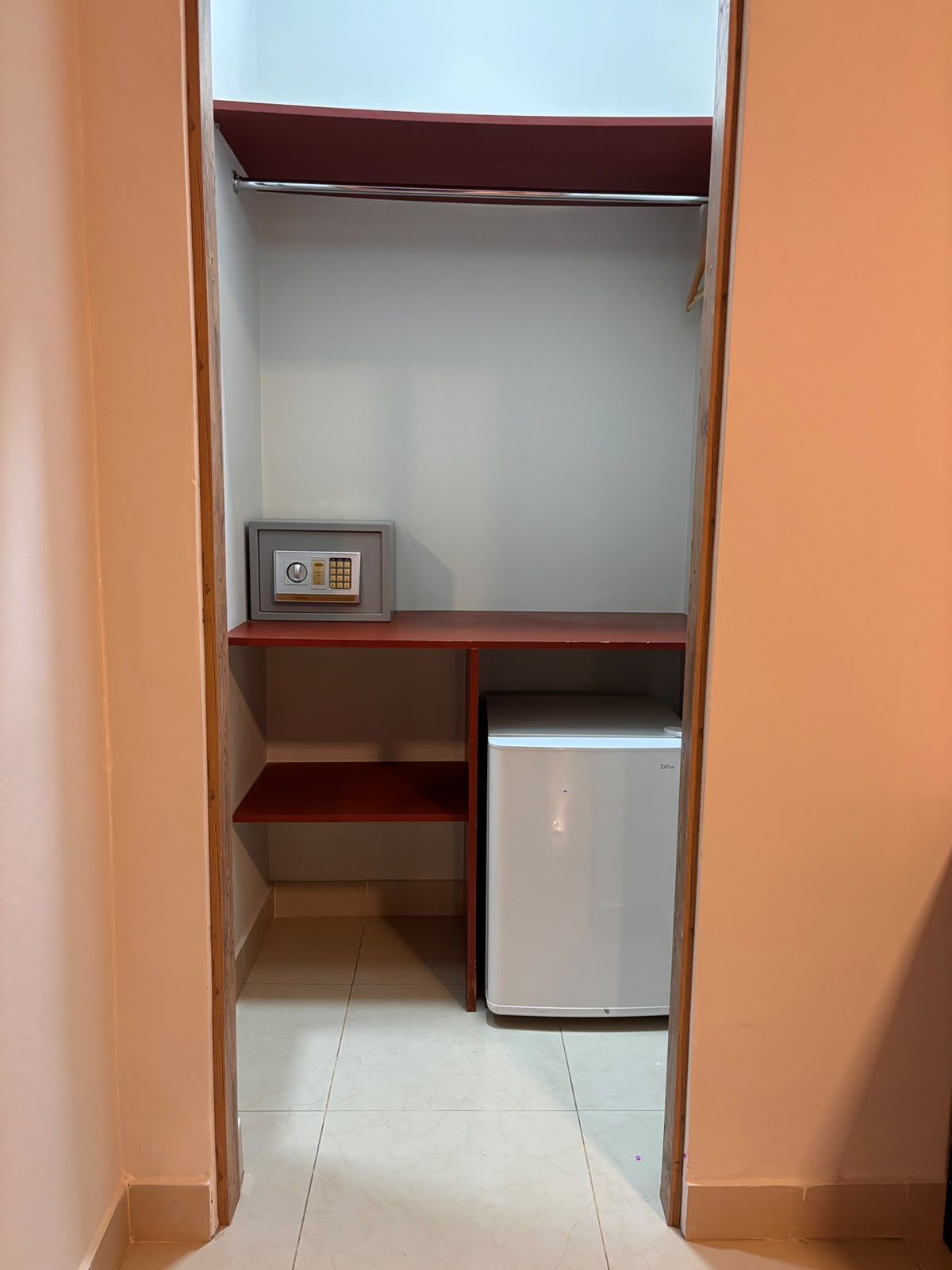 A small, enclosed space with a white refrigerator, a shelf with a small appliance, and a door leading to another room.