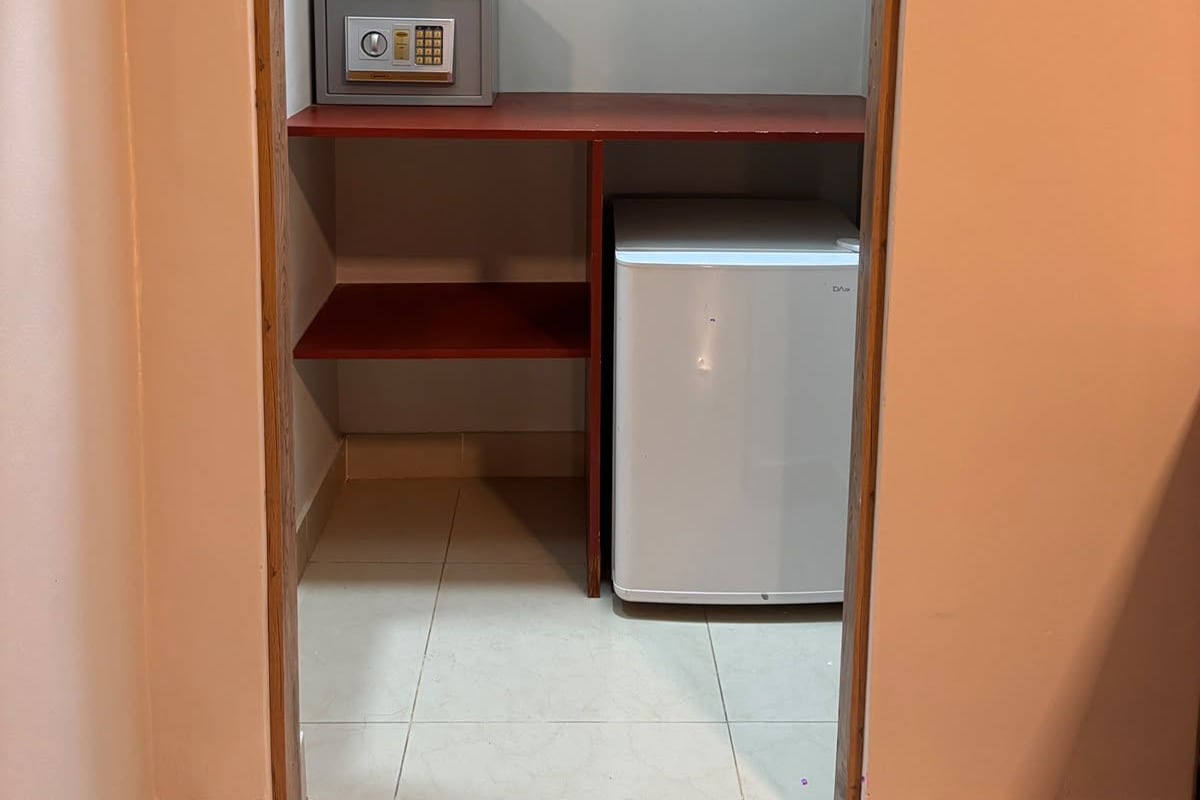 A small, enclosed space with a white refrigerator, a shelf with a small appliance, and a door leading to another room.