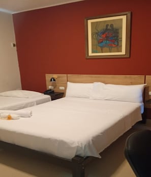A hotel room with a double bed, a single bed, a nightstand with a lamp, and a painting on the wall.