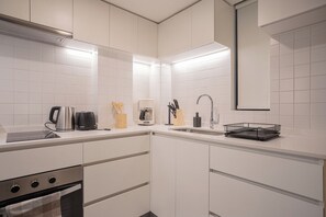 Cozinha moderna com armários brancos, forno embutido, cafeteira e pia.