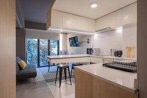 A modern kitchen with a central island, a dining area with a sofa and chairs, and a large window providing a view of greenery. - Study with a large window · Featured design (H06) (Providencia)