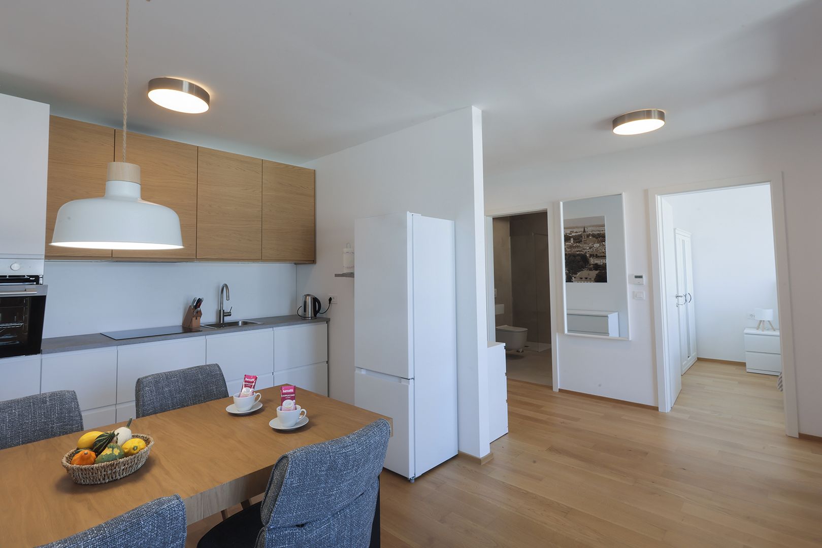 A modern kitchen with a dining area, wooden cabinets, and a white refrigerator.