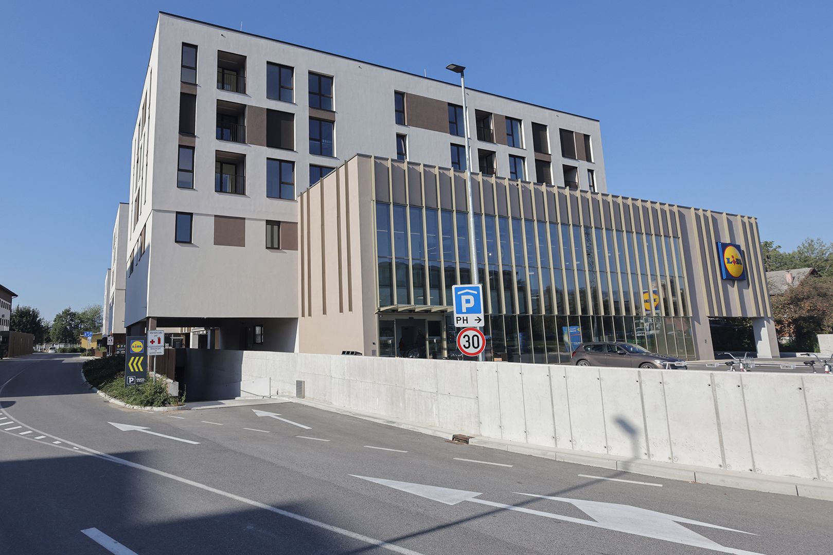 A modern building with a parking sign, a speed limit sign, and a directional arrow on the road.