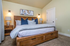 Un dormitorio con una cama de madera, dos mesitas de noche con lámparas, un cabecero con un panel decorativo y una puerta.