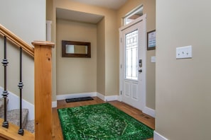 A hallway with a wooden staircase, a green rug, a door with a window, and a wall-mounted mirror. - Spacious SLC Home | Hot Tub, Game Room, BBQ & Yard (Salt Lake City)