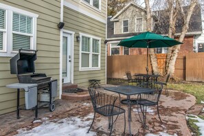 An outdoor patio with a grill, a table with chairs, and a green umbrella. - Spacious SLC Home | Hot Tub, Game Room, BBQ & Yard (Salt Lake City)