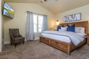 A bedroom with a large bed, a chair, a window with curtains, and a wall-mounted TV. - Spacious SLC Home | Hot Tub, Game Room, BBQ & Yard (Salt Lake City)