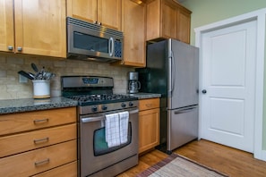 Una cocina con armarios de madera, estufa de acero inoxidable, microondas, refrigerador y cafetera.