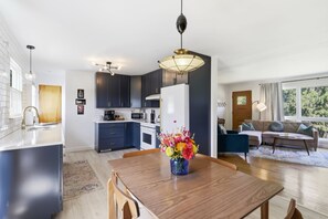 Une cuisine moderne avec des meubles de couleur sombre, un îlot central et un coin repas comprenant une table et des chaises en bois.