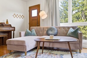 A cozy living room with a sofa, a coffee table, a lamp, and a piano. - Mid Century-Modern Retreat Great Allegheny Passage (Cresaptown, MD)