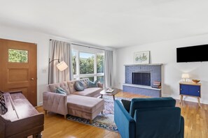Un salon comprenant un canapé, une table basse, une cheminée, un téléviseur et une porte.